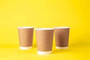 Sarı arka planda üç adet tek kullanımlık bardak. Eko kavramı, plastik yok..