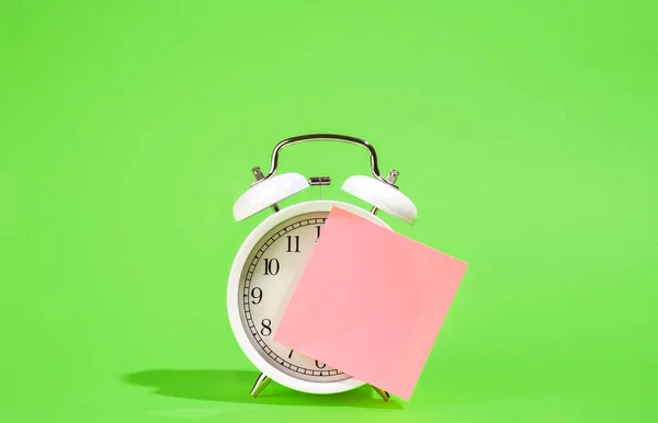 Λευκό Ξυπνητήρι Και Κενό Ροζ Χαρτί Υπενθύμισης Ένα Πράσινο Φόντο — Φωτογραφία Αρχείου