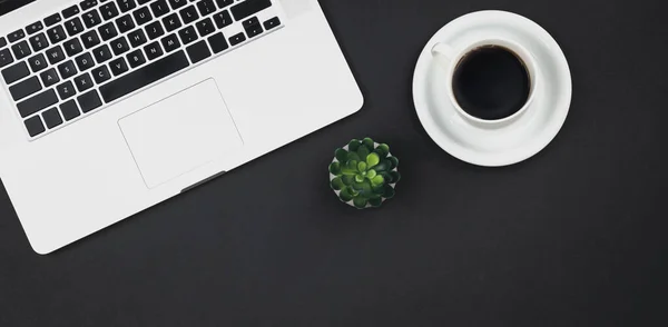 Laptop, coffee cup and office plant on black background, top view, copy space.
