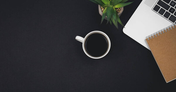 Laptop, coffee cup and notepad on black background, top view, copy space, Office work concept.