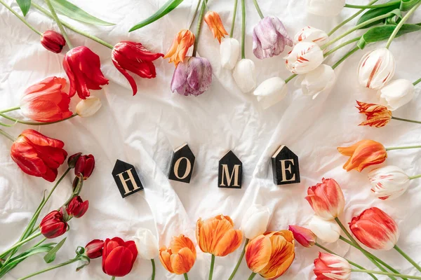 stock image Spring background with flowers tulips and decorative word Home in a white bed, top view.