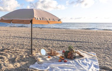 Plaid with fruits on the sandy seashore, summer picnic by the sea at sunset.