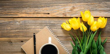 Sarı lale buketi, bir fincan kahve ve ahşap arka planda bir not defteri..