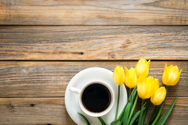 Bir buket parlak sarı lale ve bir fincan koyu kahve ahşap arka planda, üst manzara, kopyalama alanı.