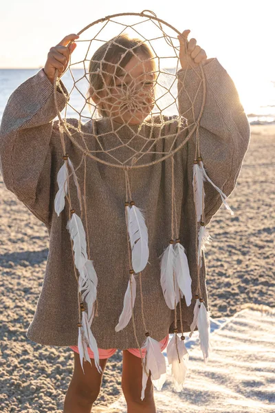 Stock image Funny little girl with a dream catcher on the seashore at sunset.