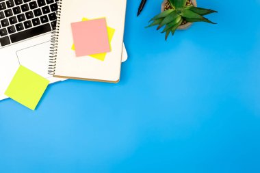 Mavi arkaplan üzerine dizüstü bilgisayar, not defteri ve kağıt hatırlatıcıları, düz yatış, iş konsepti, kopyalama alanı.