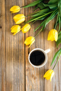 Bir buket parlak sarı lale ve bir fincan koyu kahve ahşap arka planda, üst manzara, kopyalama alanı.