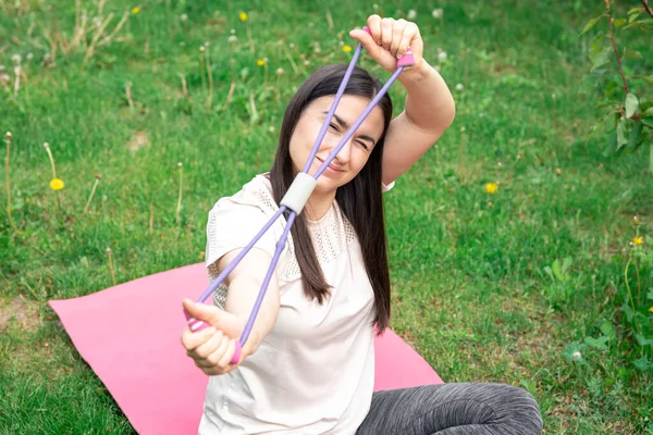 A young woman exercising with fitness band outdoors on blurred grass background.