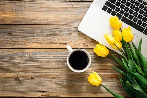 stock image Laptop, a cup of coffee and a bouquet of tulips on a wooden background, top view.