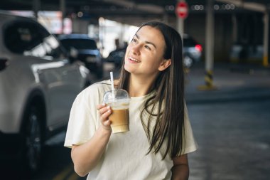 Araba parkında bir fincan kahveyle neşeli genç bir kadın..