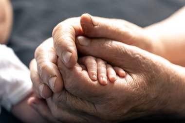 Yaşlı bir insanın elinde yeni doğmuş bir bebeğin eli, yakın plan, yumuşak odaklı..