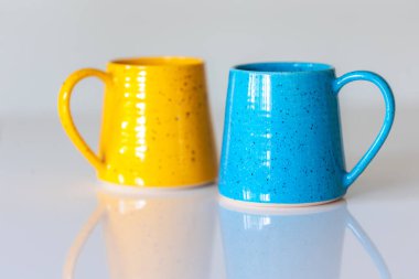 Sarı ve mavi seramik bardaklar beyaz arka planda yakın plan.