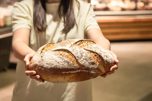 stock image A loaf of freshly baked bread in female hands in a bakery.