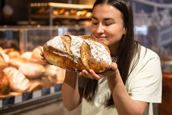 Stock image A woman smells the smell of freshly baked bread in a bakery.