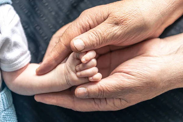 stock image The hand of a newborn baby in the hand of an old person, close-up, soft focus.