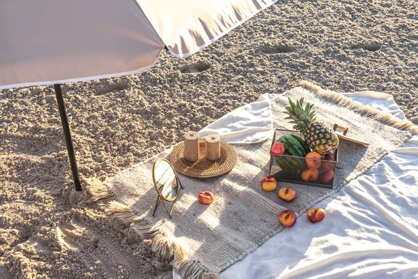 Plaid with fruits on the sandy seashore, summer picnic by the sea at sunset.