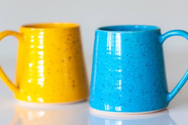 Sarı ve mavi seramik bardaklar beyaz arka planda yakın plan.