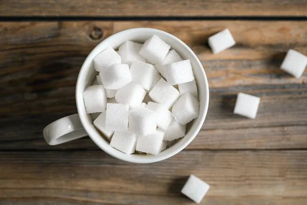 Cup with sugar cubes on a wooden surface, close-up, pressed refined sugar, diabetes, sweet drinks concept.