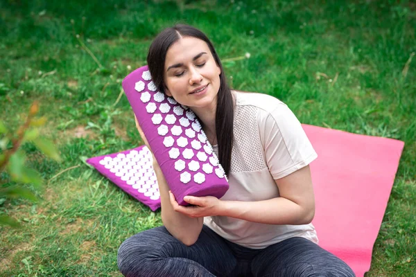 Close up, massage acupuncture mat with pillow and white massage tips, massage mat for relaxation and treatment in female hands in the garden.