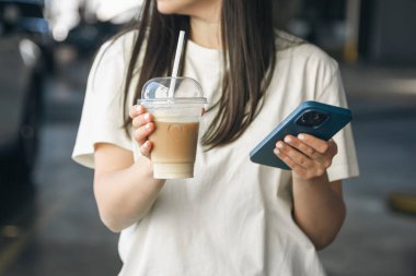 Bir fincan kahve ve bir akıllı telefon bir otoparkın arka planında kadınların elinde..