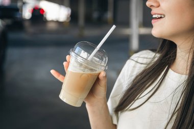 Yakın plan, bir otoparkın bulanık arka planında tek kullanımlık buzlu kahve, yaz içkisini soğutmak..
