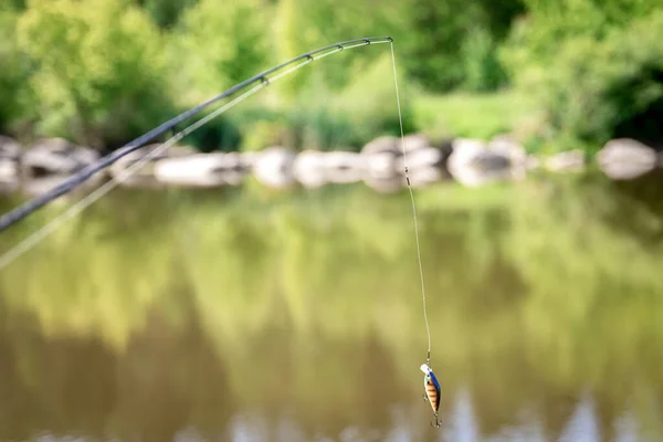 Stock image spinning reel on river bank, fishing for pike, perch, carp on beach lake or pond, background wild nature.