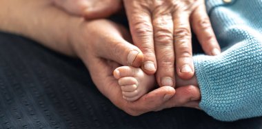 Yaşlı kadın çocuğun bacaklarını elinde tutuyor, buruşuk eller de bebeği tutuyor..