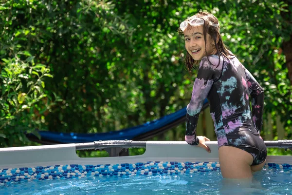 Funny little girl in the pool in the backyard with swimming goggles, copy space.