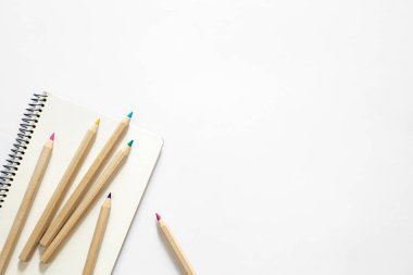 Farklı renklerde tahta kalemler ve beyaz arkaplanda bir defter, üst görünüm, boşluk kopyala.