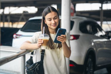 Akıllı telefonlu neşeli bir genç kadın ve otoparkta bir şey, taksi, turizm ve yaşam tarzı konsepti bekleyen bir kadın..