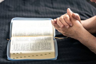 Evde, İncil 'in önünde dua etmek için katlanmış yaşlı bir kadının elleri yatağın üzerinde..