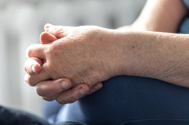 Yakın plan, yaşlı bir kadının elleri, elleri bağlı oturan yaşlı bir kadın..