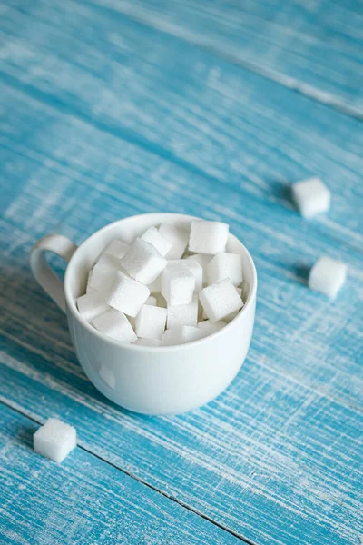 Cup with white sugar cubes on a blue wooden surface, close-up, pressed refined sugar, diabetes, sweet drinks concept.