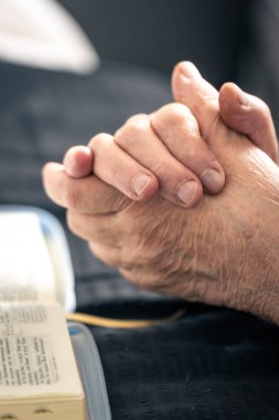 Evde, İncil 'in önünde dua etmek için katlanmış yaşlı bir kadının elleri yatağın üzerinde..