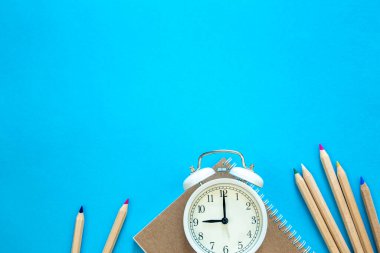 Alarm saati, not defteri ve mavi arka planda kalemler, üst görünüm, okul ve çalışma konsepti.