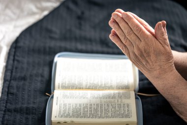 Evde, İncil 'in önünde dua etmek için katlanmış yaşlı bir kadının elleri yatağın üzerinde..