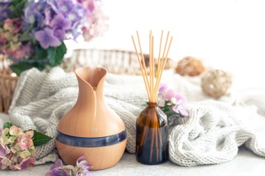 Aroma yağı yayıcı lamba, çiçekler ve bulanık arka planda örülmüş elementi içeren spa kompozisyonu, boşluğu kopyala.