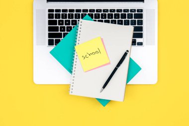Laptop ve not defteri sarı arka plan, üst görünüm, okul çalışma konsepti.