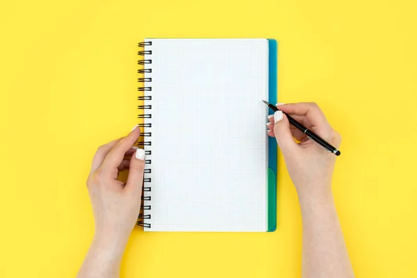 スパイラルノートで書く女性の手の写真のトップビューコピースペースと黄色の背景にパッド — ストック写真