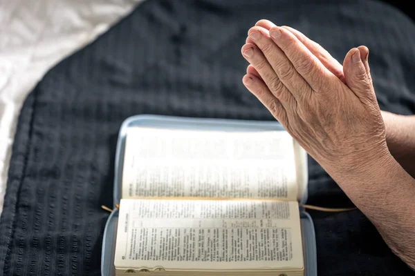 Evde, İncil 'in önünde dua etmek için katlanmış yaşlı bir kadının elleri yatağın üzerinde..