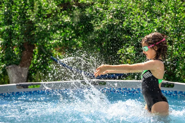A girl splashes in an inflatable pool in the garden on a sunny summer day.