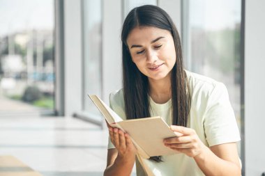 Yazın güneşli bir günde pencerenin kenarında oturup kitap okuyan çekici bir genç kadın..