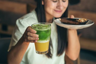 Yakın plan, limonata ve çikolatalı kek bir kafede kadınların ellerinde..