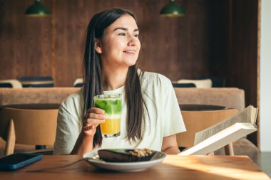 Kafede bir bardak limonatayla kitap okuyan çekici genç bir kadın. Lezzetli bir yaz atıştırmalığı..