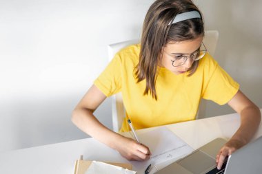 Ev ödevi yapan genç bir kız kitap ve dizüstü bilgisayarla oturuyor, çevrimiçi öğrenim konsepti, evde okuyan bir çocuk, yer kopyalıyor..