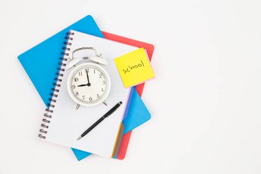 Not defterleri, bir çalar saat ve beyaz arka plan üzerine bir kağıt hatırlatma, üst görünüm, okul konsepti.