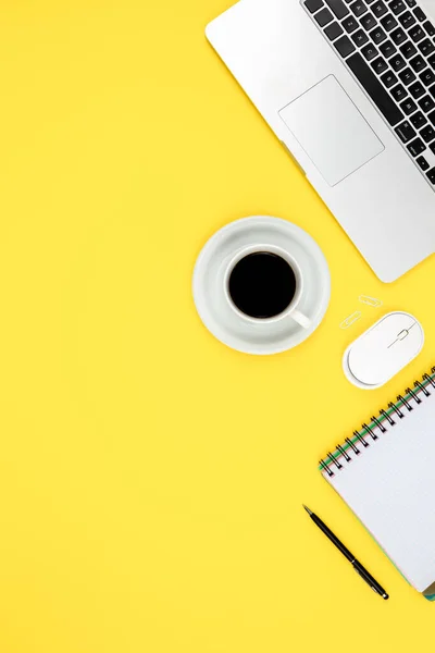 Work space desk layout with notepad, laptop and coffee cup on a yellow background, modern office desk.