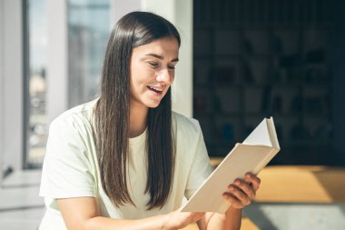 Yazın güneşli bir günde pencerenin kenarında oturup kitap okuyan çekici bir genç kadın..