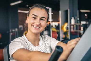 Spor salonunda spor giyimli güzel bir esmer kadın bisiklete biniyor, sağlıklı bir yaşam tarzı..