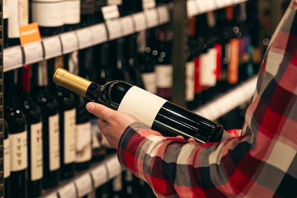 A man holding a wine bottle in a liquor wine shop, choosing the right wine from all the variations of wine bottles on the shelves.